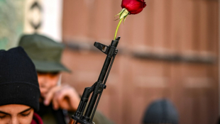 Une rose est placée dans le canon d'un fusil d'assaut tenu par un combattant syrien avant la prière hebdomadaire à la mosquée des Omeyyades à Damas, le 13 décembre 2024 ( AFP / Aris MESSINIS )