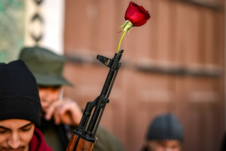 Une rose est placée dans le canon d'un fusil d'assaut tenu par un combattant syrien avant la prière hebdomadaire à la mosquée des Omeyyades à Damas, le 13 décembre 2024 ( AFP / Aris MESSINIS )