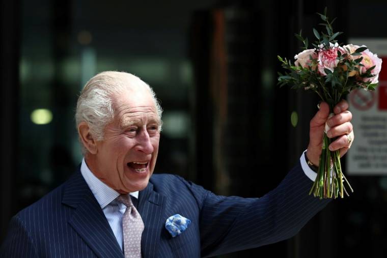 Le roi Charles III brandit un bouquet de fleurs qu'on lui a offert, au cours d'une visite dans un centre de traitement du cancer, à Londres, le 30 avril 2024 ( AFP / HENRY NICHOLLS )