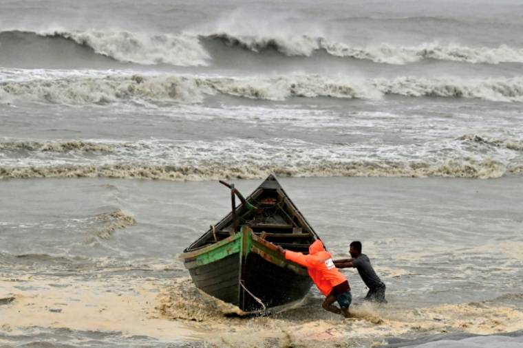 Des hommes poussent un bateau de pêche à titre préventif lors des pluies à Kuakata le 26 mai 2024, avant l'arrivée du cyclone Remal dimanche soir au Bangladesh.  ( AFP / Munir UZ ZAMAN )