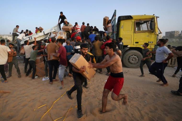Des Palestiniens transportent des cartons d'aide humanitaire après s'être hués sur des camions arrivés près de Nousseirat, dans le centre de la bande de Gaza, le 18 mai 2024 ( AFP / - )