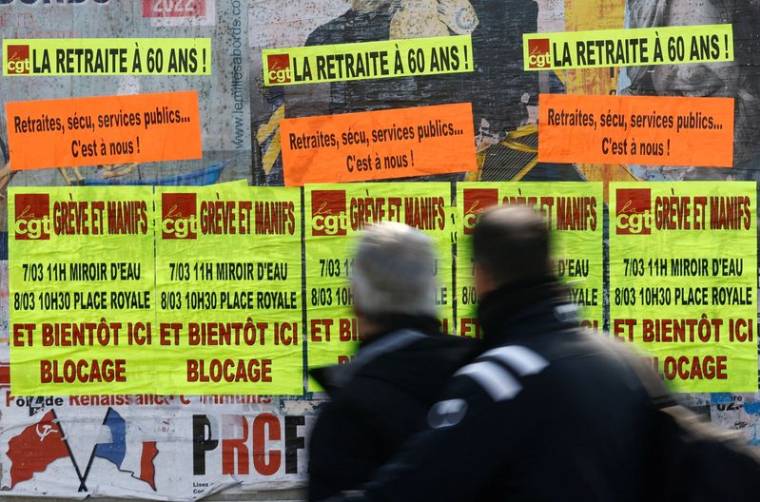 Des gens passent devant des affiches à Bouguenais appelant à la grève et à des manifestations contre le plan de réforme des retraites du gouvernement