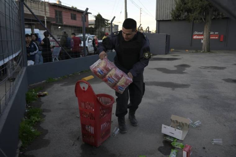 Un policier récupère des marchandises abandonnées sur un parking après le pillage d'un supermarché, le 22 août 2023 à José C. Paz, faubourg populaire près de Buenos Aires, en Argentine ( AFP / Juan MABROMATA )
