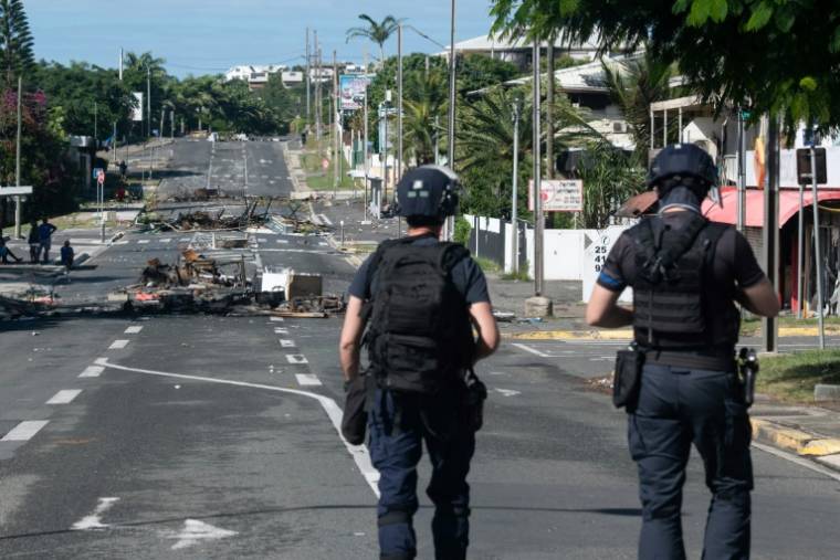 Des policiers en patrouille sur une rue bloquée par des objets incendiés et des débris, dans le quartier Magenta à Nouméa en Nouvelle-Calédonie, le 18 mai 2024 ( AFP / Delphine Mayeur )