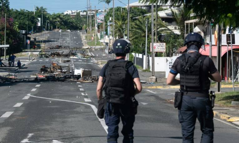 Des policiers en patrouille sur une rue bloquée par des objets incendiés et des débris, dans le quartier Magenta à Nouméa en Nouvelle-Calédonie, le 18 mai 2024 ( AFP / Delphine Mayeur )