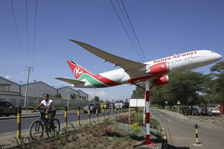 Une femme passe en vélo à côté de la maquette d'un appareil aux couleurs de Kenya Airways, devant le siège de la compagnie, à Nairobi le 6 février 2024 ( AFP / Tony KARUMBA )