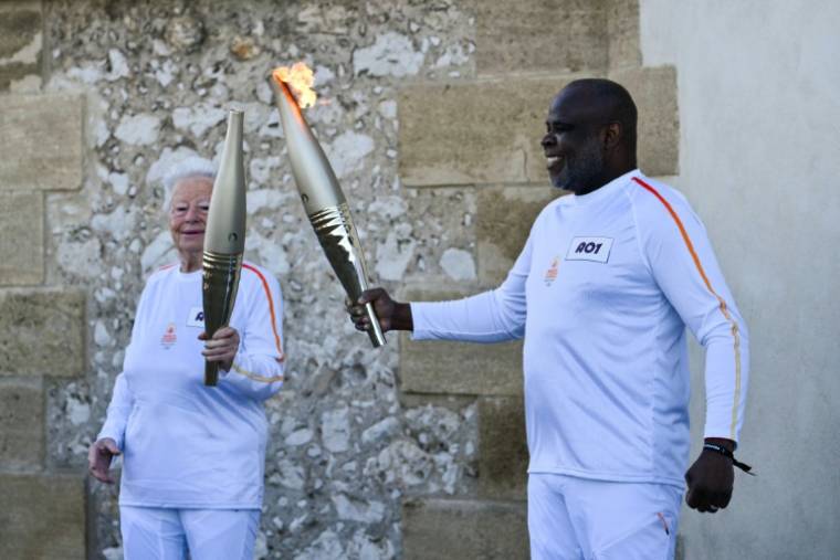 L'ancien footballeur français Basile Boli (d) allume le flambeau de Colette Cataldo, supportrice historique de l’OM, dans le cadre des relais de la flamme olympique et paralympique à la basilique Notre Dame de la Garde, à Marseille, le 9 mai 202 ( AFP / CHRISTOPHE SIMON )