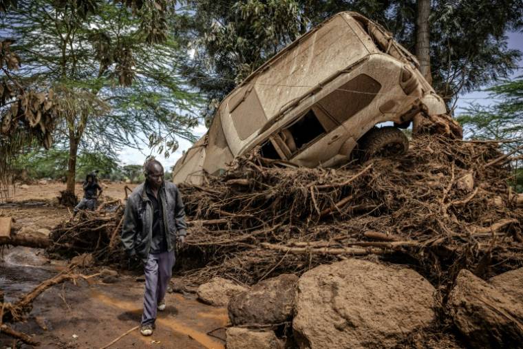Un homme passe près d'une voiture emportée par l'inondation dans le village de Kamuchiri (Kenya), près de Mai Mahiu, le 29 avril 2024 ( AFP / LUIS TATO )