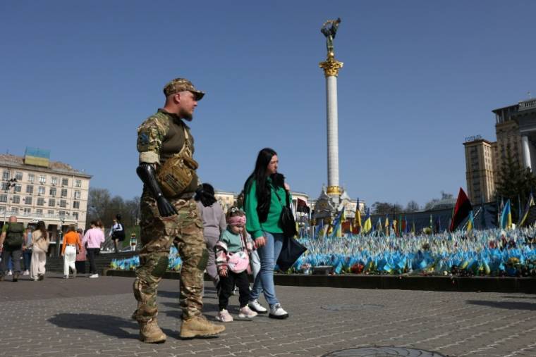 Le sergent Valeriï Koutcherenko, équipé d'une prothèse bionique, passe avec sa femme Veronika et sa fille Oleksandra, devant un mémorial pour les soldats ukraniens tombés au combat, place de l'Indépendance à Kiev, le 2 avril 2024 ( AFP / Anatolii STEPANOV )