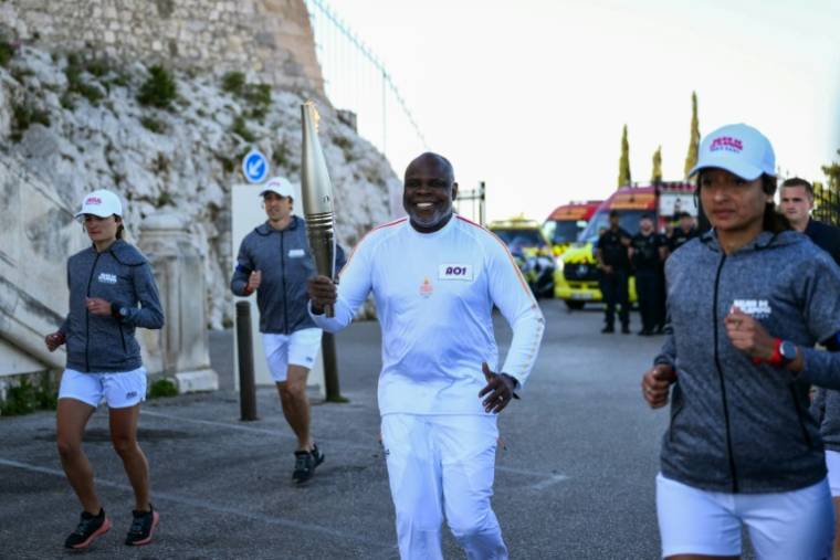 L'ancien footballeur français Basile Boli court avec la flamme olympique à la basilique Notre-Dame de la Garde, à Marseille, dans le cadre des relais de la flamme olympique et paralympique, le 9 mai 2024 ( AFP / CHRISTOPHE SIMON )