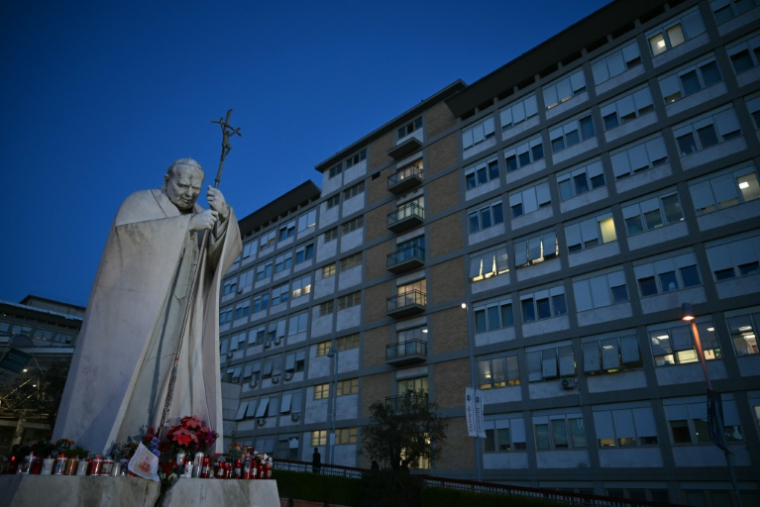 Des bougies sont posées au pied de la statue de Jean Paul II devant l'hôpital Gemelli où se trouve le pape François, à Rome, le 22 février 2025 ( AFP / Alberto PIZZOLI )