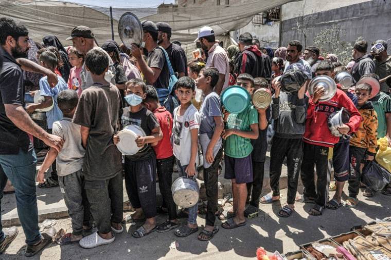 Des hommes, des femmes et des enfants font la queue pour recevoir des rations alimentaires à Deir el-Balah, dans le centre de la bande de Gaza, le 13 mai 2024 ( AFP / - )