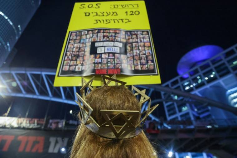 Une manifestante porte sur sa tête une couronne sur laquelle est accrochée une pancarte avec les photos des otages retenus à Gaza avec l'inscription "Sortez les de l'enfer", lors d'un rassemblement à Tel-Aviv, le 29 juin 2024 ( AFP / JACK GUEZ )
