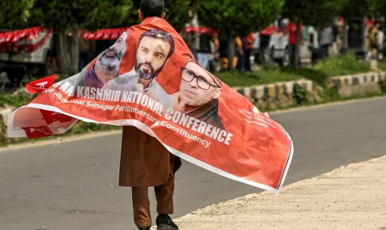 Un partisan de la Conférence Nationale porte une bannière avec des photos de dirigeants du parti lors d'un meeting de campagne électorale à Srinagar, la principale ville du Cachemire administrée par l'Inde, le 11 mai 2024 ( AFP / TAUSEEF MUSTAFA )