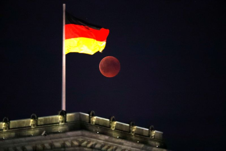 La lune est visible à côté du drapeau allemand au sommet du bâtiment du Reichstag