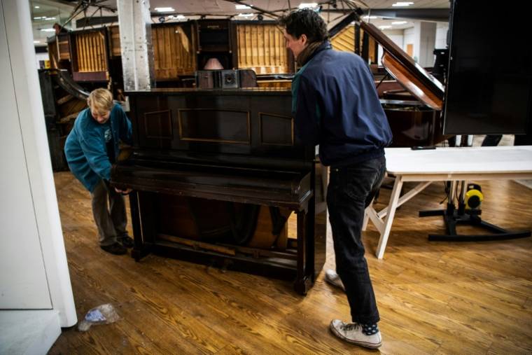 Des bénévoles déplacent un vieux piano dans l'atelier de "Pianodrome", le 9 février 2023 à Edimbourg, en Ecosse ( AFP / Andy Buchanan )