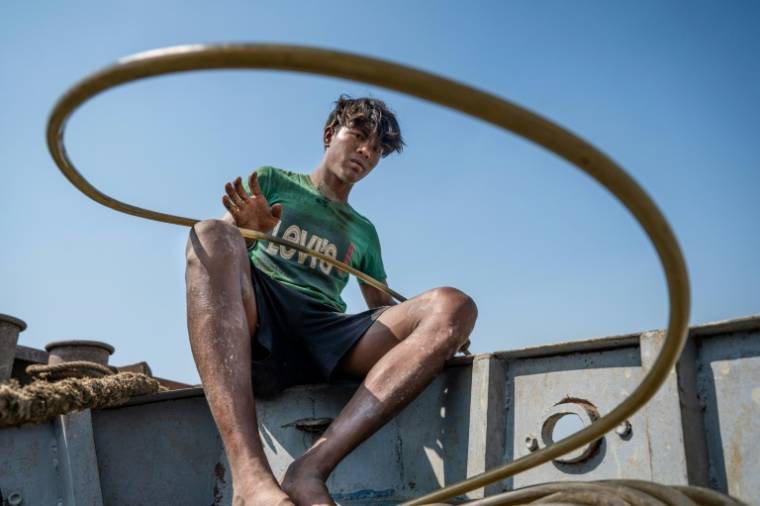 Un homme tient un tuyau d'oxygène en caoutchouc pendant que des plongeurs récupèrent un navire coulé dans le fleuve Yangon, le 23 janvier 2024 à Rangoun, en Birmanie ( AFP / Sai Aung MAIN )