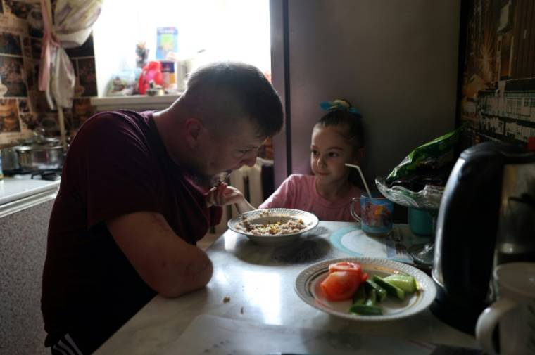 Valeria, fille aînée du sergent ukrainien Valeriï Koutcherenko, aide son père à manger avec une fourchette, dans leur appartement à Bila Tserkva, au sud de Kiev, le 4 avril 2024 ( AFP / Anatolii STEPANOV )