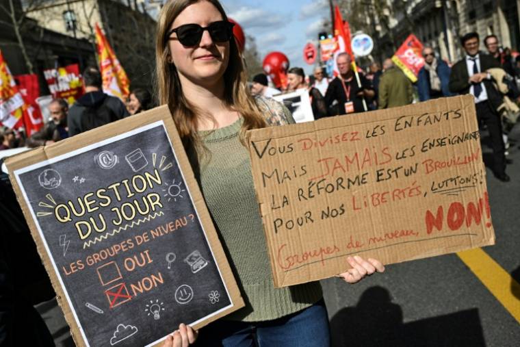 Une personne tient deux pancartes contre les groupes de niveau lors d'une manifestation le 19 mars 2024 à Paris ( AFP / Bertrand GUAY )