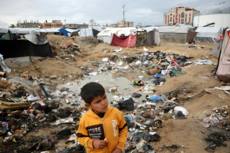 Un enfant gazaoui au milieu de déchets et eaux stagnantes dans un camp de déplacés à  Nousseirat, dans le centre de la bande de Gaza, le 23 février 2025 ( AFP / Eyad BABA )