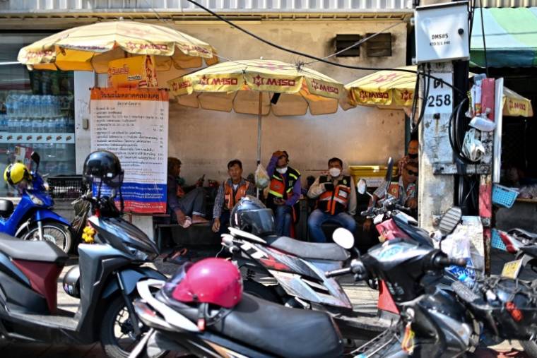 Des chauffeurs de taxi-moto s'abritent du soleil sous des parasols en attendant des clients, le 25 avril 2024 à Bangkok, en Thaïlande où une vague de chaleur extrême est attendue ( AFP / MANAN VATSYAYANA )