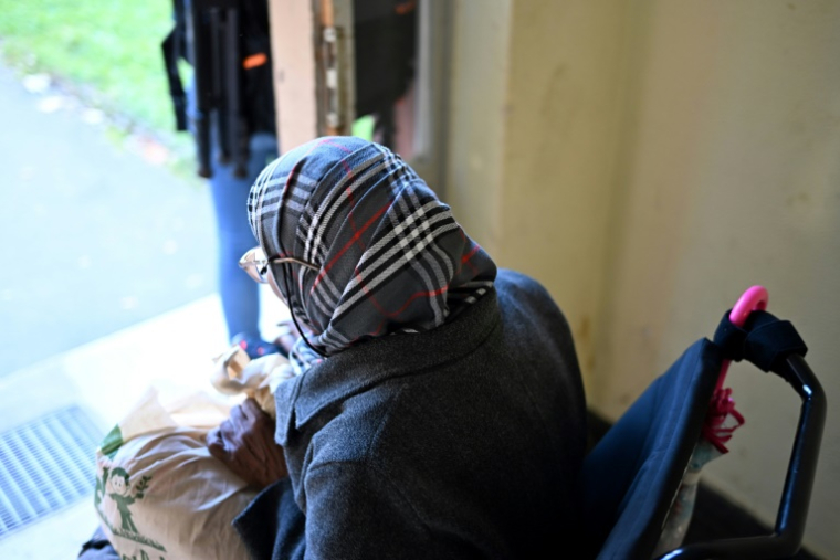 Une femme âgée en fauteuil roulant quitte un bâtiment du foyer temporaire pour réfugiés et demandeurs d'asile  situé sur le site de l'ancien camp d'accueil d'urgence pour les réfugiés et les réinstallés de la RDA à Marienfelde, dans la banlieue de Berlin, le 16 octobre 2024 ( AFP / Ralf Hirschberger )