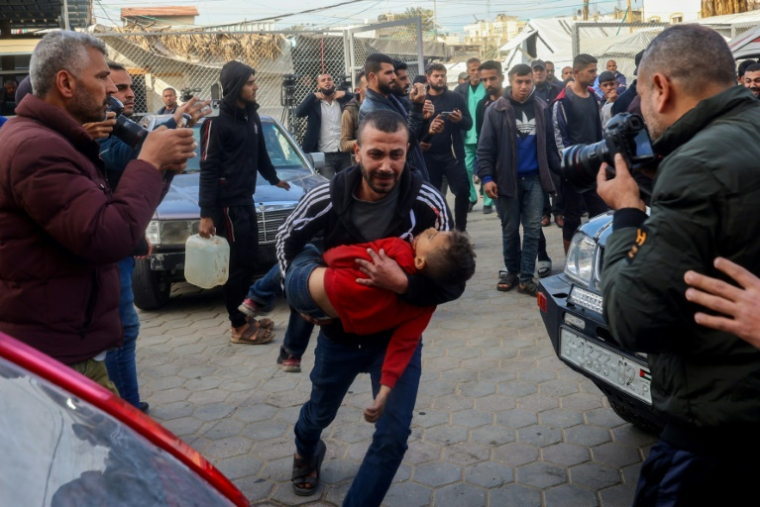 Un Palestinien porte un enfant blessé dans un hôpital après une meurtrière frappe israélienne sur Deir el-Balah, dans le centre de la Bande de Gaza, le 14 janvier 2025 ( AFP / Eyad BABA )