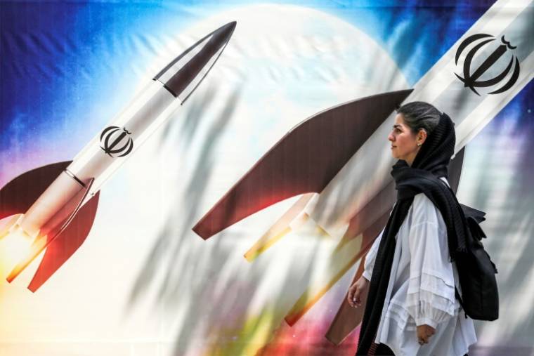 Une femme marche près d'un poster géant montrant des missiles avec l'emblême de la République islamique dans le centre de Téhéran, le 15 avril 2024 ( AFP / ATTA KENARE )
