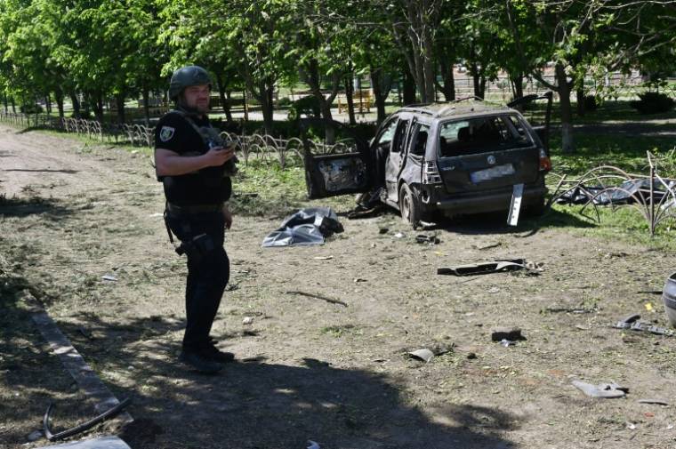 Un policier ukrainien près d'une voiture détruite par une frappe russe à  Zlotchiv, dans la région de Kharkiv, le 1er mai 2024 ( AFP / SERGEY BOBOK )