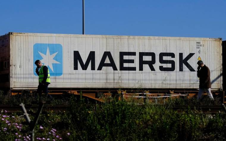 Des travailleurs parlent sur leur téléphones portables, alors qu'un conteneur Maersk est transporté par un train, près du port de Barcelone