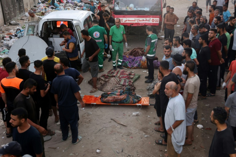 Des Palestiniens déplacés regardent les premiers intervenants se préparer à transporter les corps des personnes tuées lors de frappes israéliennes sur une école de la ville de Gaza, le 10 août 2024 ( AFP / Omar AL-QATTAA )