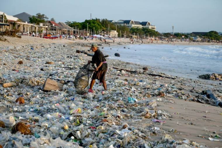 Un homme ramasse des objets recyclables pour les vendre au milieu de plastiques et d'autres débris échoués sur la plage de Kedonganan, dans la zone touristique de Kuta, sur l'île de Bali, en Indonésie, le 19 mars 2024 ( AFP / SONNY TUMBELAKA )