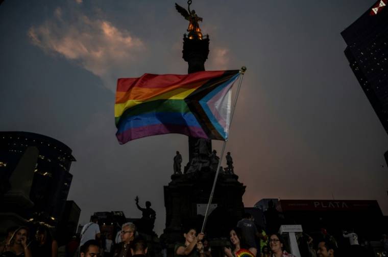 Un homme agite le drapeau arc-en-ciel, symbole de la communauté LGBT+, devant l'ange de l'Indépendance dans le centre de Mexico le 16 mai 2024 pour la journée contre l'homophobie, lesbophobie, transphobie et la biphobie ( AFP / Yuri CORTEZ )
