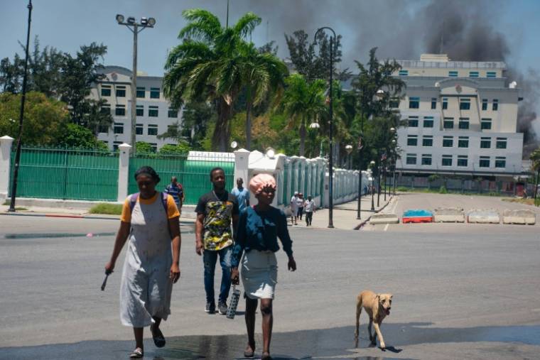 De la fumée s'échappe d'un bâtiment du ministère des Finances, alors que des habitants quittent les lieux après avoir entendu des tirs, le 2 avril 2024 à Port-au-Prince, en Haïti ( AFP / Clarens SIFFROY )