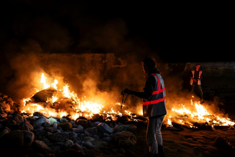 Thomas Chambon (C), coordinateur de l'association Utopia 56, et Nikolaï Posner, un bénévole et ancien salarié d'Utopia 56, près d'un canot en feu sur la plage du Portel (Pas-de-Calais) le 21 septembre 2024 ( AFP / Sameer Al-DOUMY )