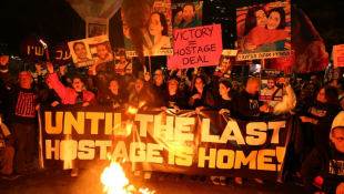 Des Israéliens tiennent des pancartes et allument des bougies  lors d'une manifestation antigouvernementale appelant à agir pour obtenir la libération des otages israéliens à Gaza, devant le ministère de la Défense à Tel-Aviv le 18 janvier 2025 ( AFP / Jack GUEZ )