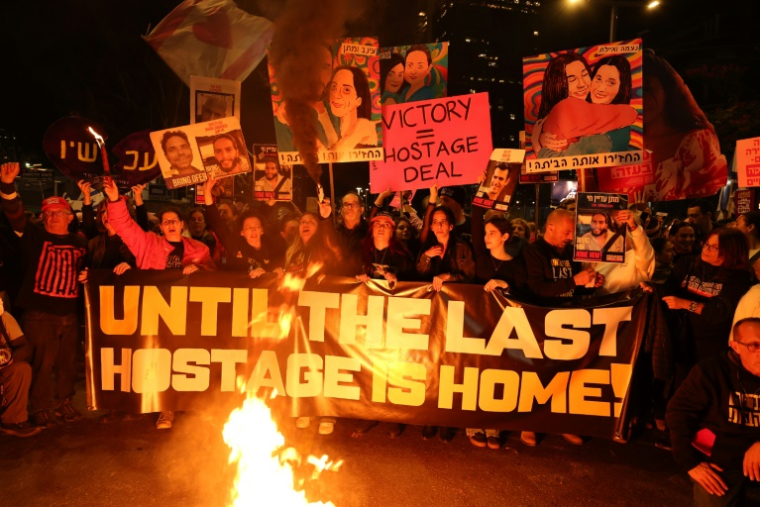 Des Israéliens tiennent des pancartes et allument des bougies  lors d'une manifestation antigouvernementale appelant à agir pour obtenir la libération des otages israéliens à Gaza, devant le ministère de la Défense à Tel-Aviv le 18 janvier 2025 ( AFP / Jack GUEZ )