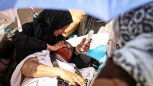 Une femme utilise un ventilateur portatif pour rafraîchir un homme allongé au sol, affecté par la forte chaleur, lors du pèlerinage annuel musulman à Mina près de la Mecque en Arabie saoudite, le 16 juin 2024 ( AFP / FADEL SENNA )