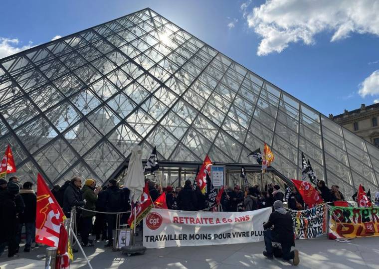 Des manifestants portant des drapeaux CGT et Sud Culture Solidaires se tiennent devant la Pyramide du Louvre