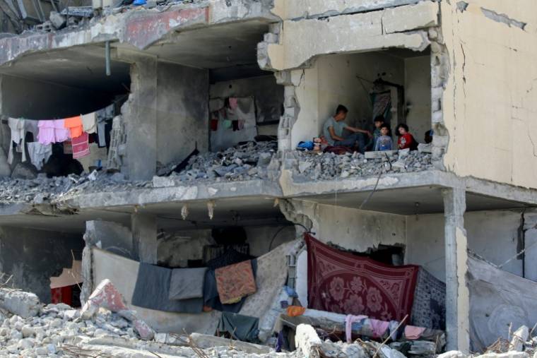 Un Palestinien et ses enfants assis dans une pièce d'une maison fortement endommagée par une  frappe aérienne israélienne à Rafah, dans le sud de la bande de Gaza, le 22 mai 2024 ( AFP / Eyad BABA )