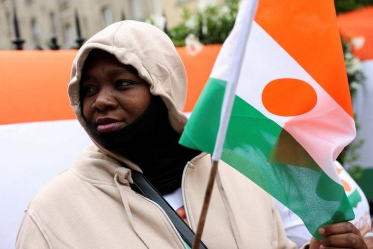Une personne tient un drapeau du Niger devant l'ambassade du Niger, à Paris