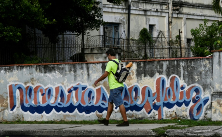 Un homme passe devant le graffiti "Necesitas ser feliz" (Tu dois être heureux) du graffeur cubain Mr. Sad, à La Havane, le 18 décembre 2024 ( AFP / YAMIL LAGE )