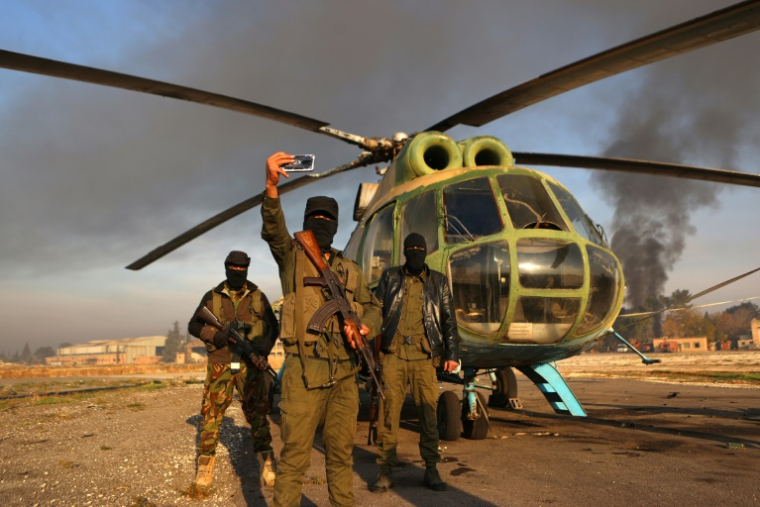 Des combattants antirégime devant  un hélicoptère de l'armée sur le tarmac de l'aérodrome militaire de Nayrab dans la ville d'Alep, dans le nord de la Syrie, le 2 décembre 2024 ( AFP / AAREF WATAD )