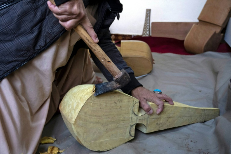 Sakhi, un artisan afghan, utilise une hachette pour fabriquer un rubab, un instrument à cordes en bois de mûrier séché provenant des déserts, dans un atelier à Herat, le 22 décembre 2024 ( AFP / Wakil KOHSAR )