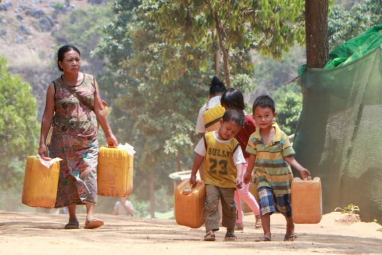 Une femme et des enfants portent des bidons remplis d'eau potable distribuée dans un camp de personnes déplacées à Demoso, dans l'État de Kayah, le 29 avril 2024 dans l'est de la Birmanie  ( AFP / STR )