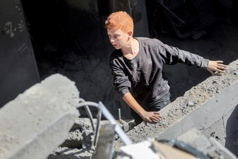 Un garçon palestinien sort des décombres d'une habitation touchée par un bombardement israélien dans la ville de Gaza, le 26 octobre 2024 ( AFP / Omar AL-QATTAA )