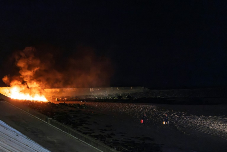 Des policiers éloignent des bidons d'essence d'un canot en feu sur la plage du Portel (Pas-de-Calais) le 21 septembre 2024 ( AFP / Sameer Al-DOUMY )