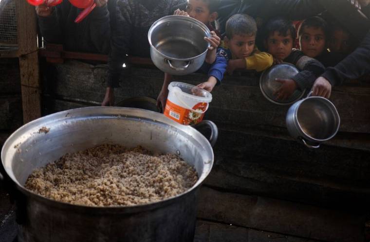Des enfants palestiniens attendent de recevoir de la nourriture préparée par une cuisine caritative dans un contexte de pénurie alimentaire, à Rafah