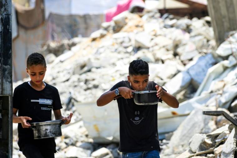 De jeunes Palestiniens transportent des casseroles de nourriture à Nousseirat, dans le centre de la bande de Gaza, le 12 juillet 2024 ( AFP / Eyad BABA )