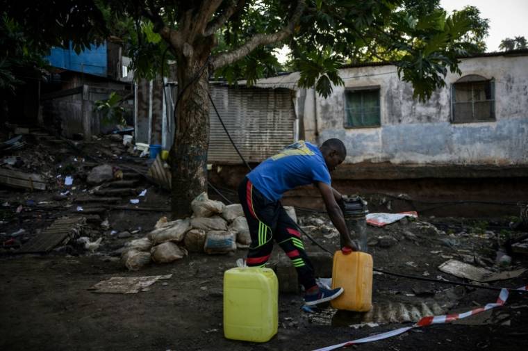Un homme remplit des bidons d'eau près du bidonville "Talus 2" à Koungou, en cours de démolition, sur l'île française de Mayotte dans l'océan Indien, le 23 mai 2023 ( AFP / PHILIPPE LOPEZ )